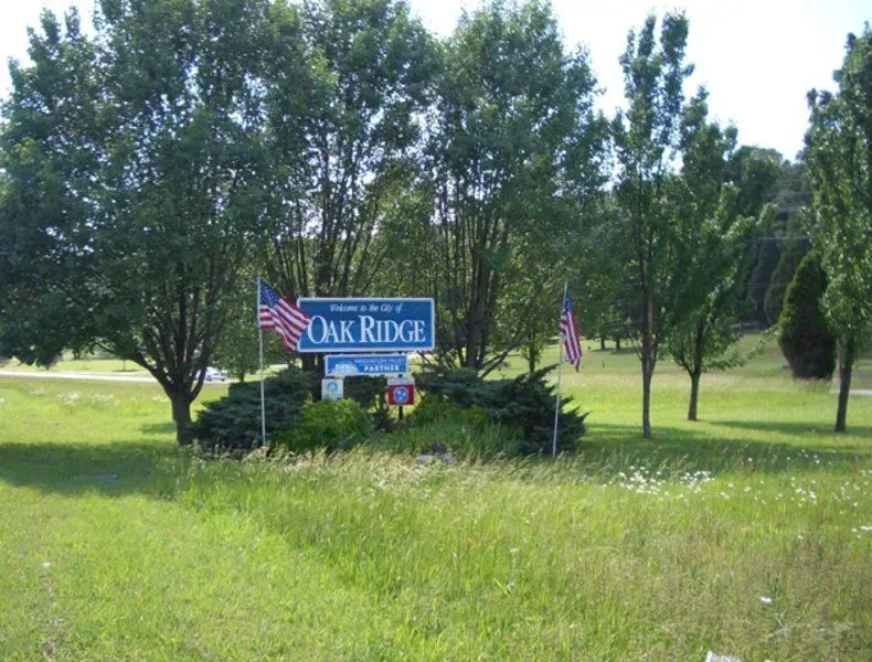 Sign for Oak Ridge, with American flags, surrounded by trees and grass.