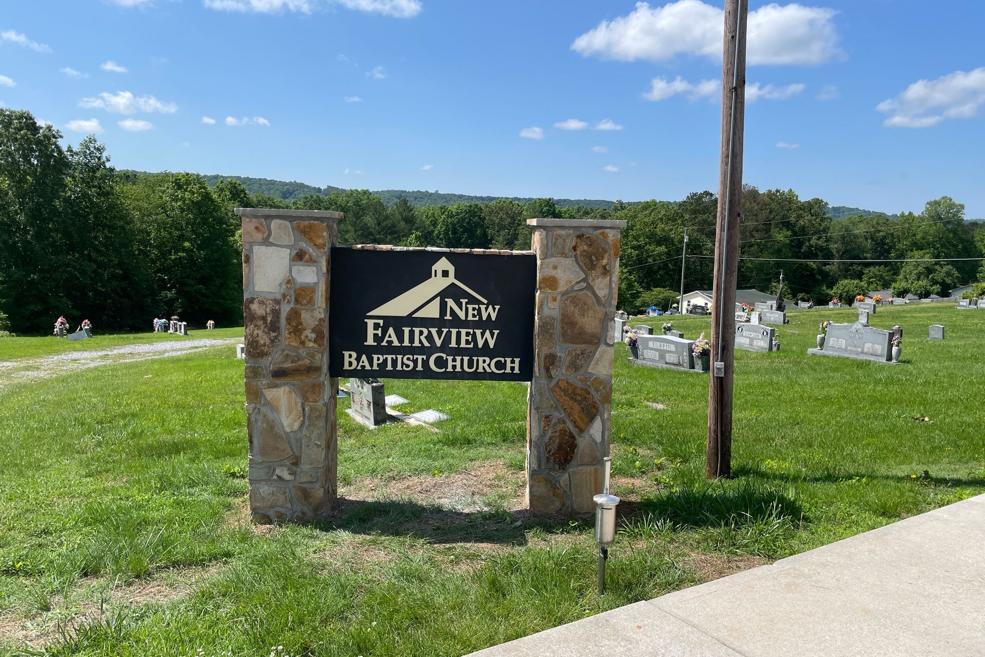 Sign for New Fairview Baptist Church in front of a cemetery, under a blue sky.