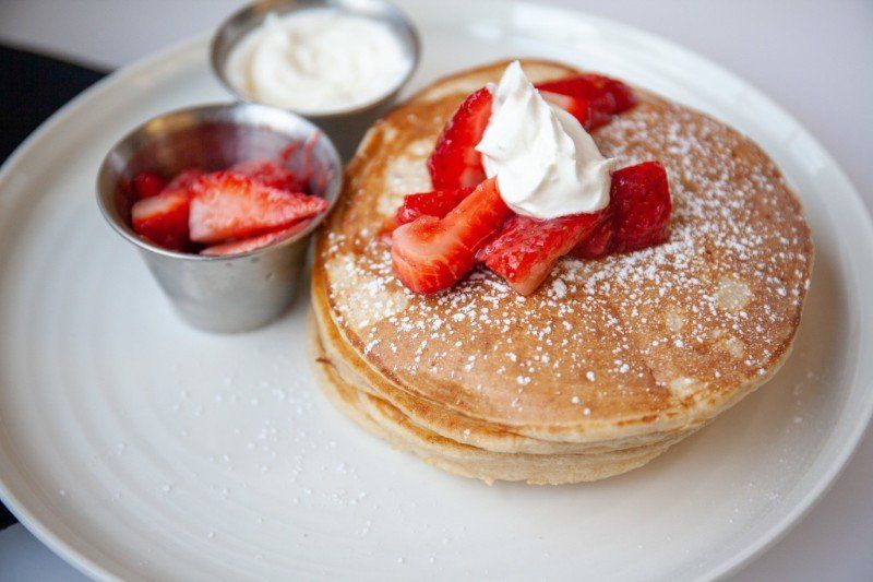 A white plate topped with pancakes with whipped cream and strawberries.