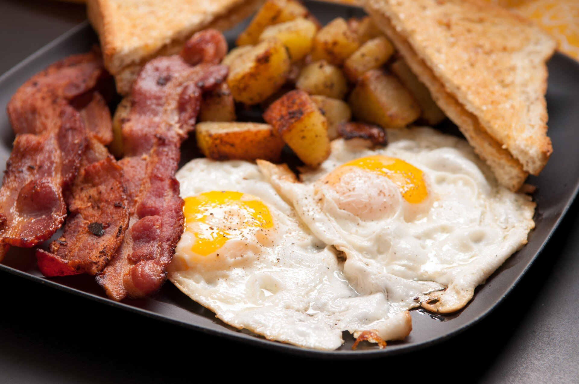 A black plate topped with eggs , bacon , potatoes and toast.