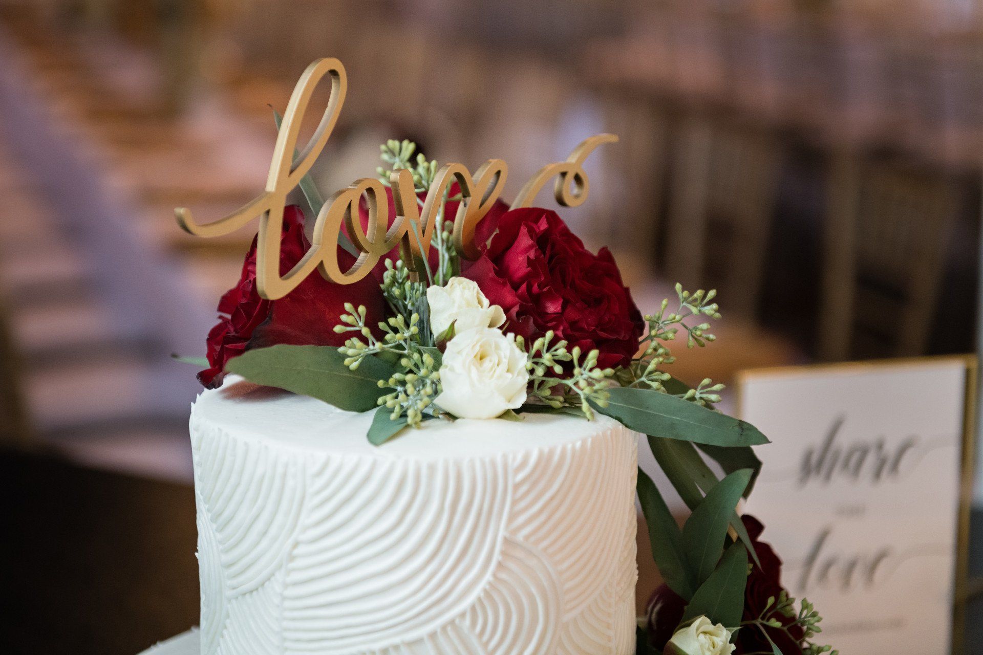 A wedding cake with flowers and a love sign on top.