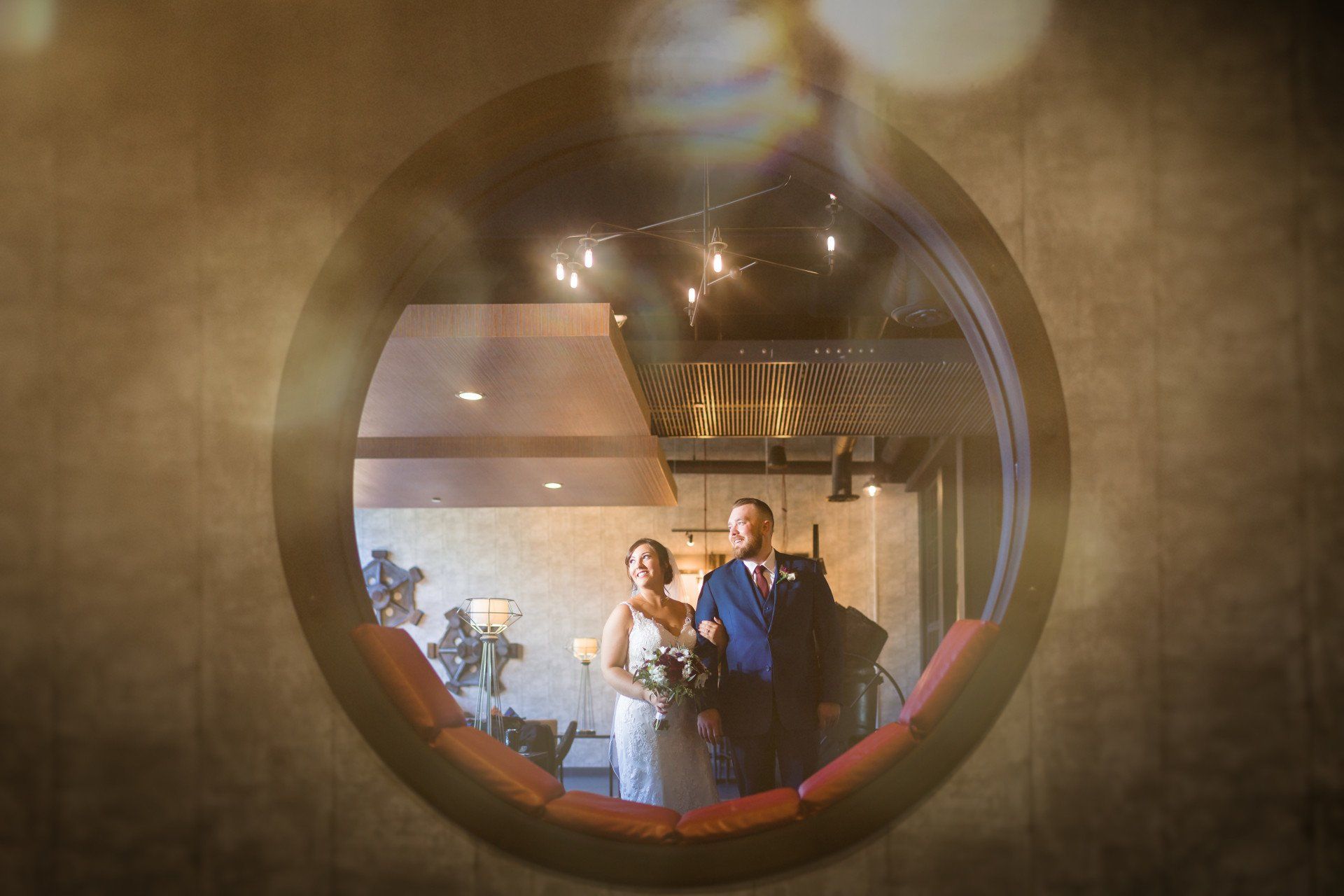 A bride and groom are standing in front of a round window.