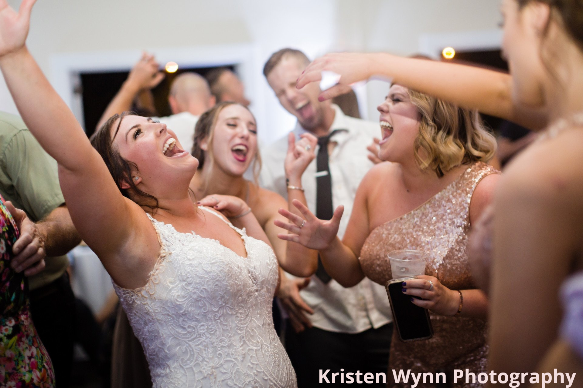A bride is dancing with her arms in the air at a wedding reception.