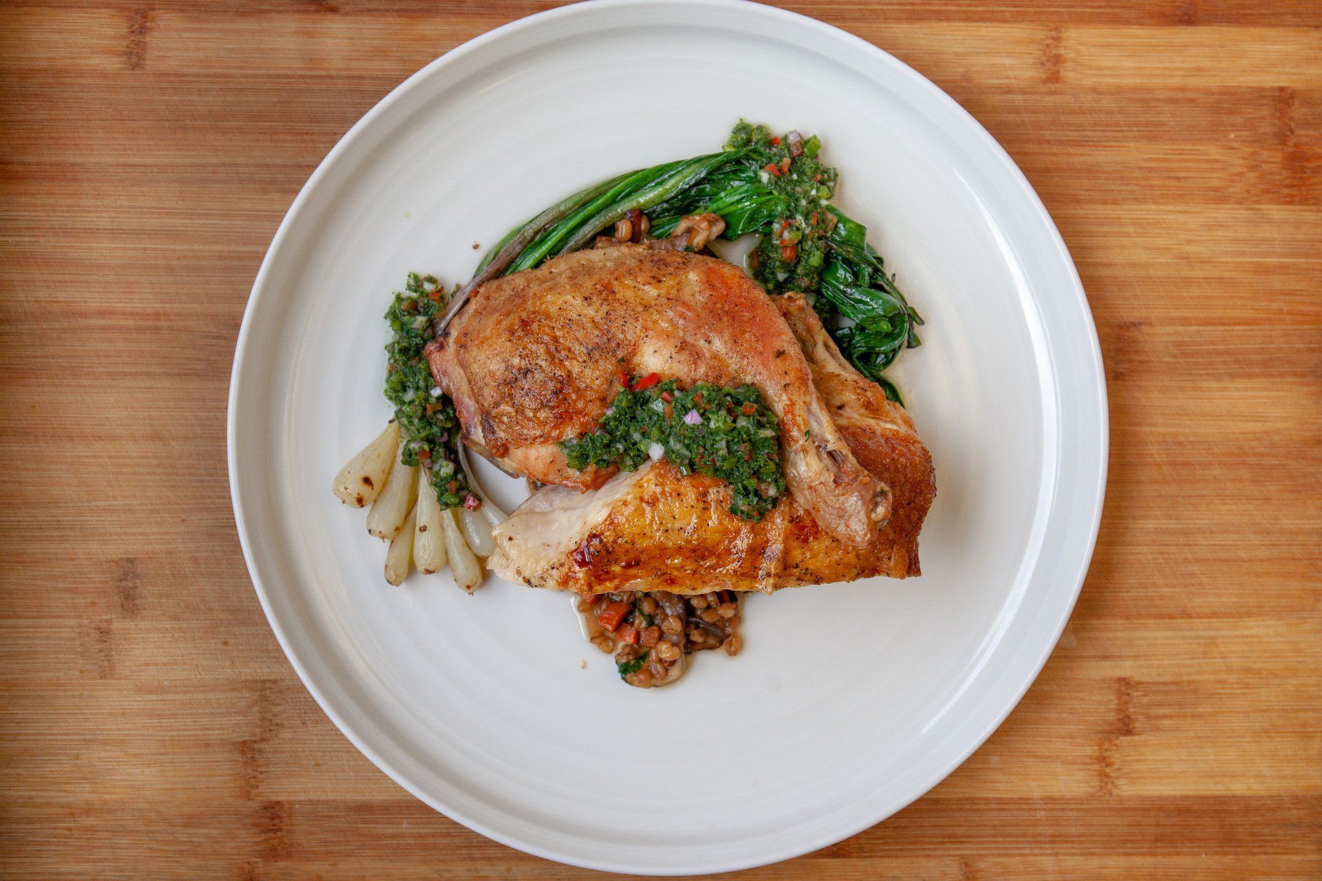 A white plate topped with meat and vegetables on a wooden table.