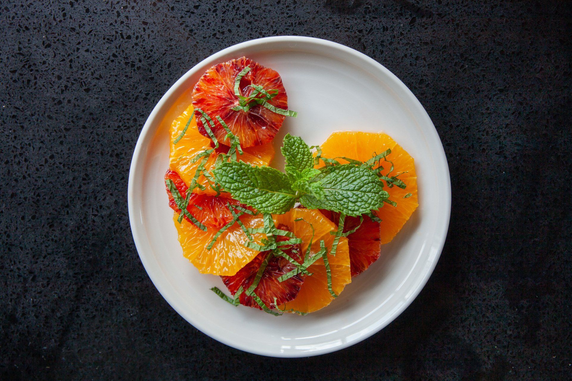 A white plate topped with sliced oranges and mint leaves.