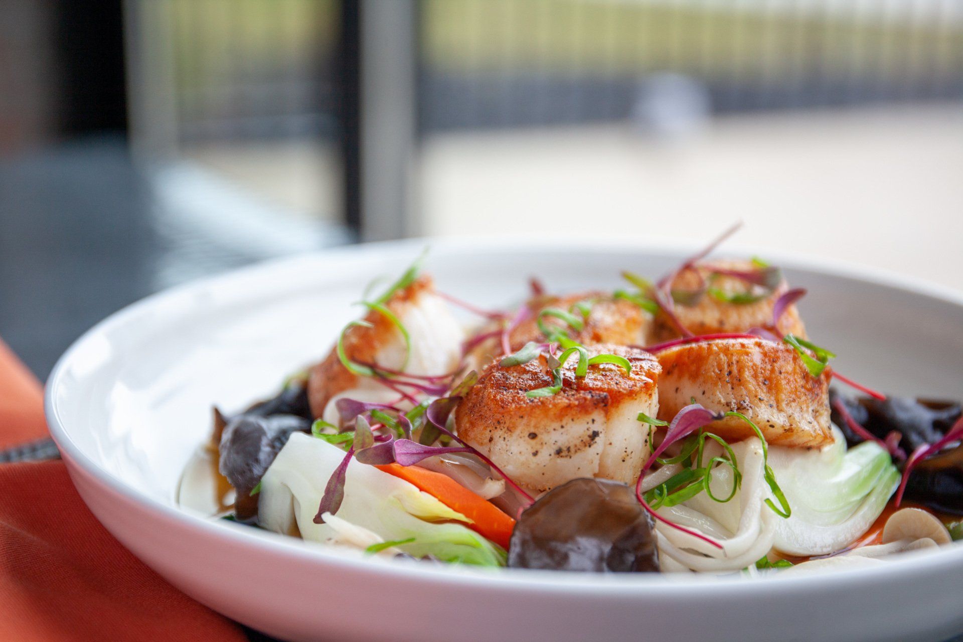 A close up of a plate of food with scallops and vegetables on a table.