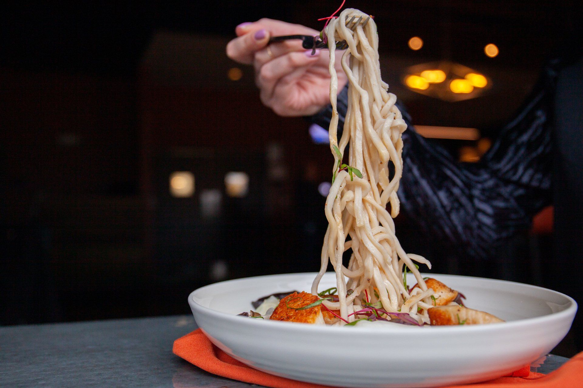 A person is eating noodles with chopsticks from a white plate.