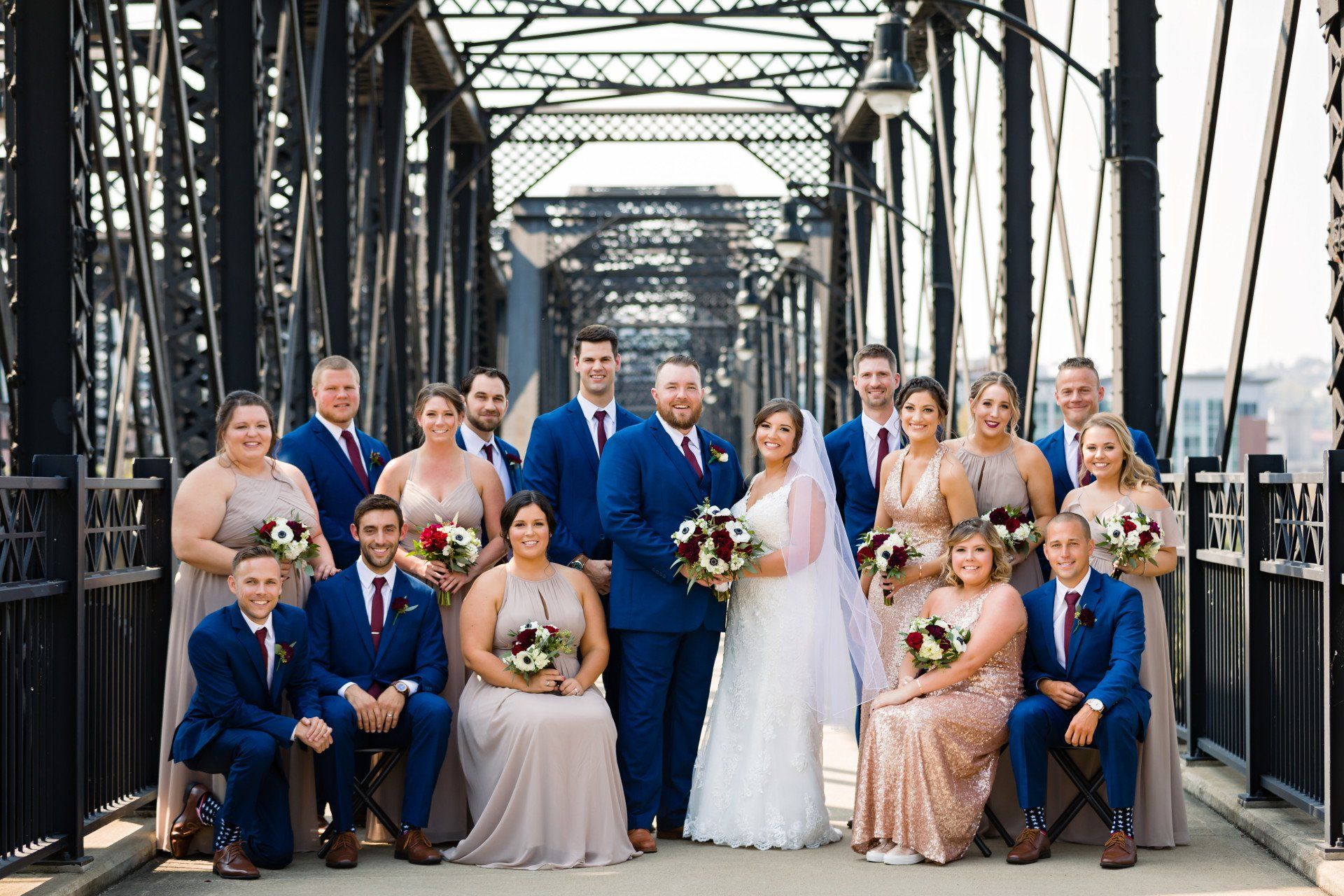 The bride and groom are posing for a picture with their wedding party on a bridge.