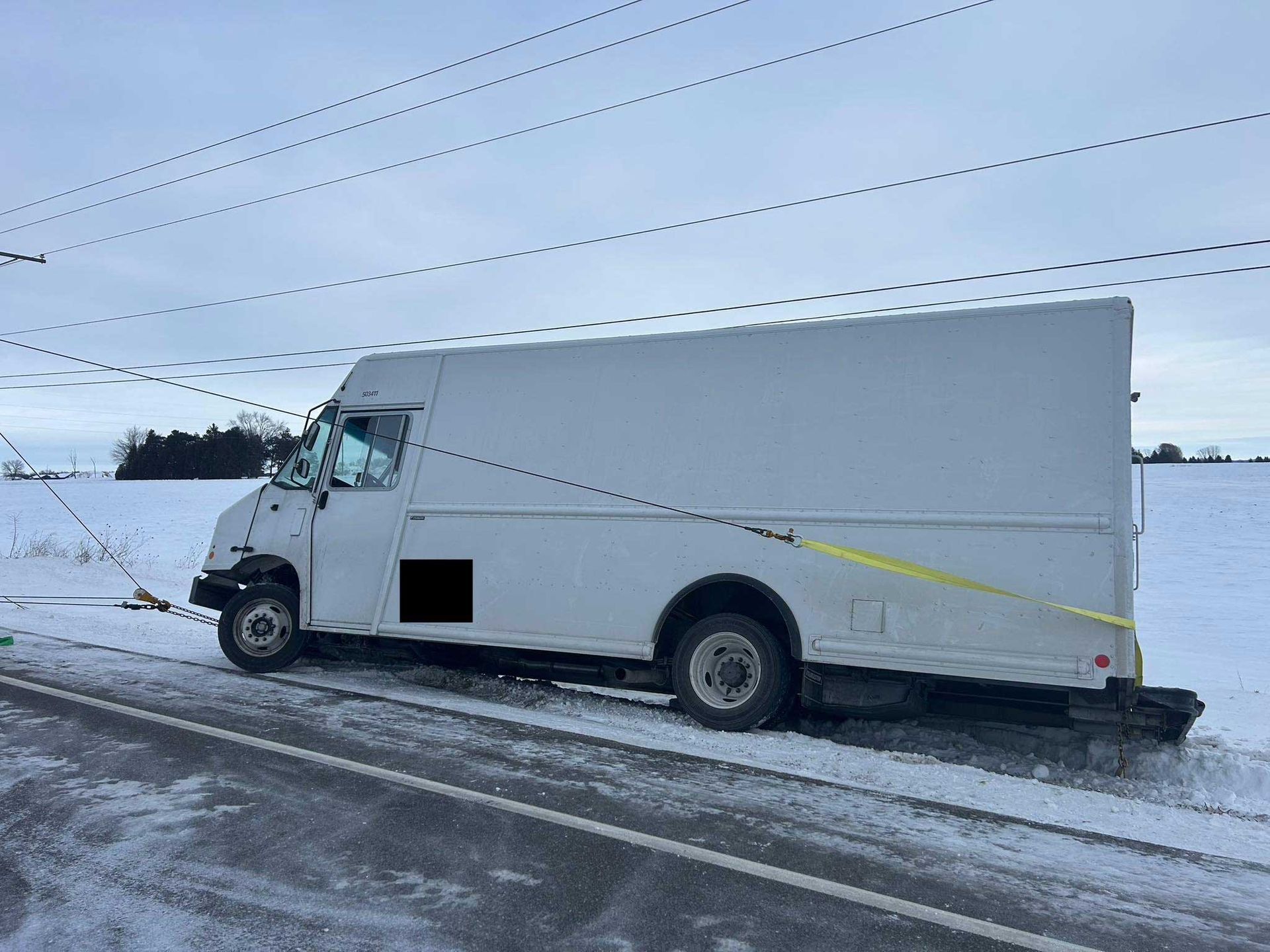 White box truck driving on a snowy road under a cloudy sky