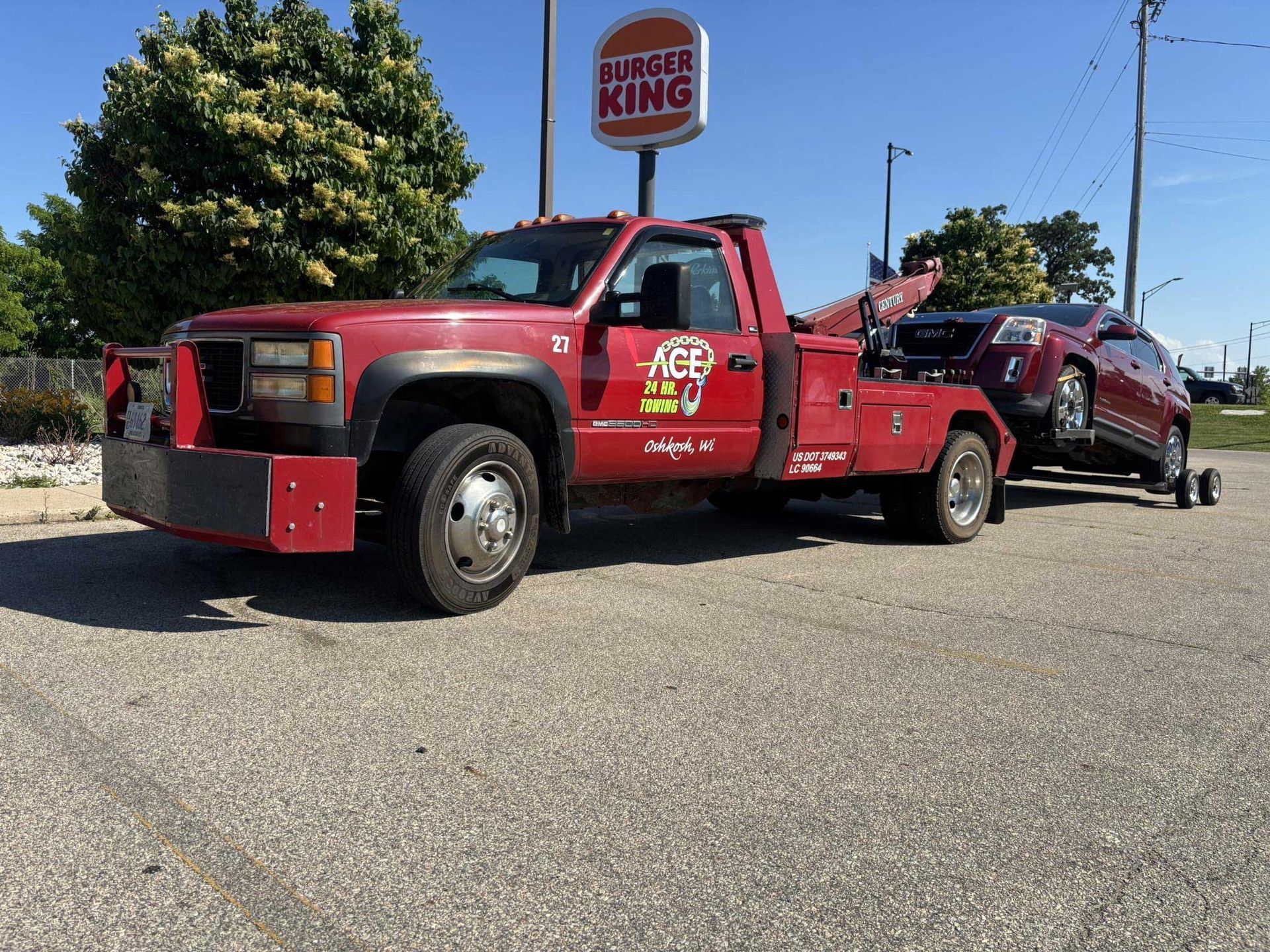 Red tow truck hauling a maroon SUV in a parking lot near a Burger King sign.