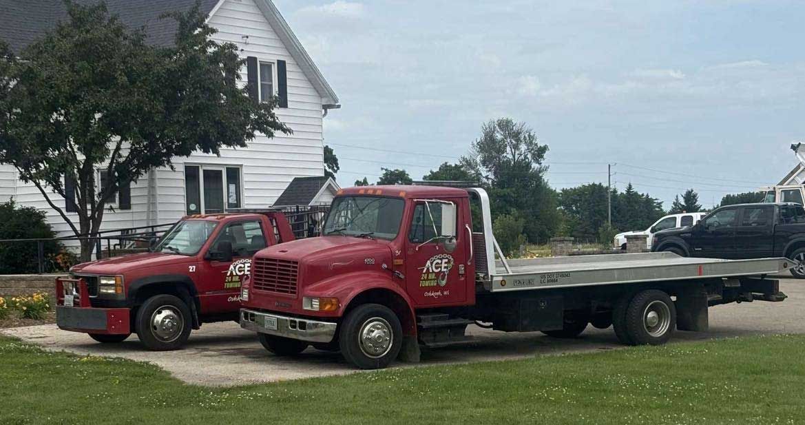 Two red tow trucks parked on grass beside a white house on a sunny day