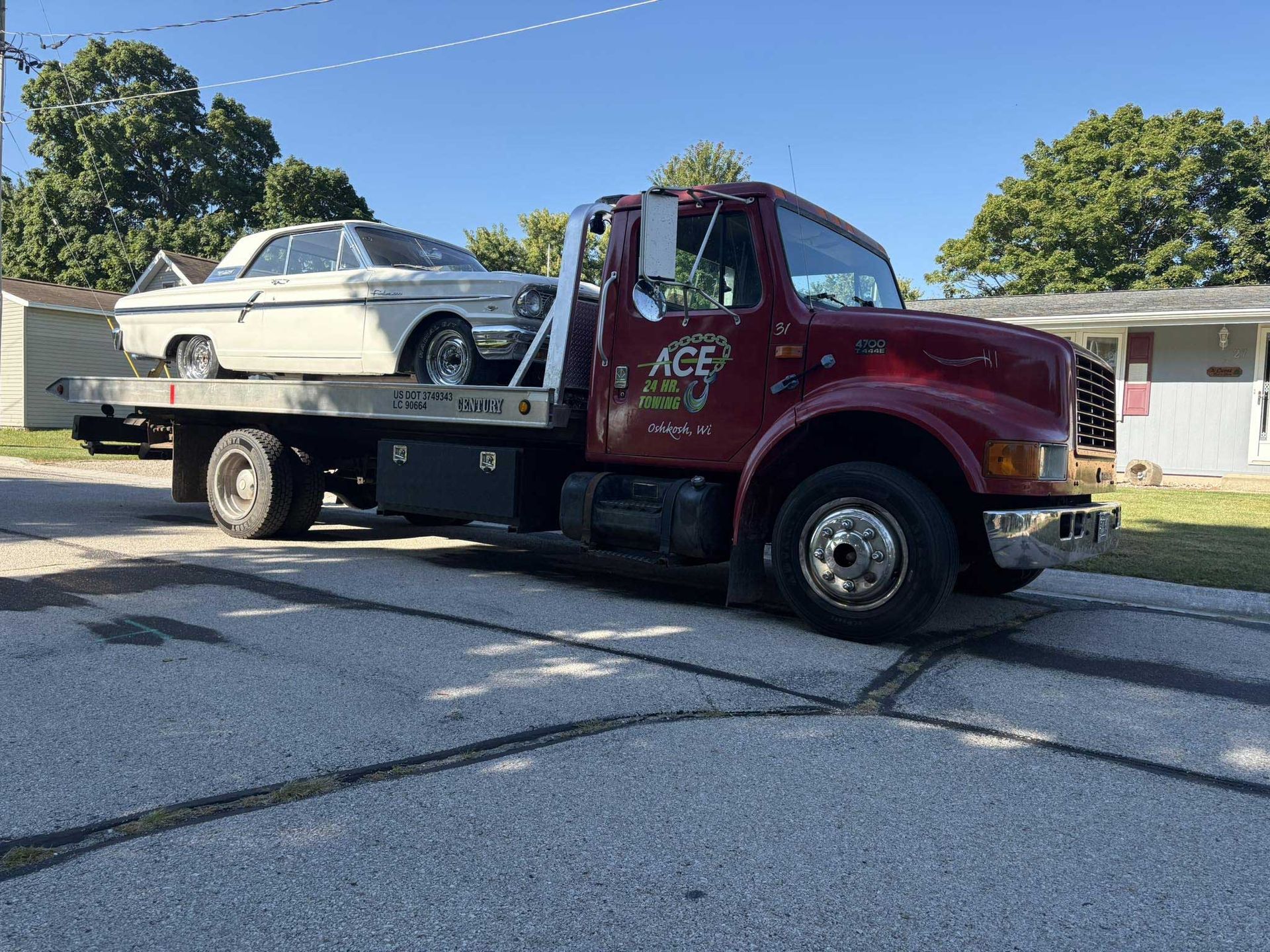Tow truck carrying a cream-colored car on a residential street under a clear sky