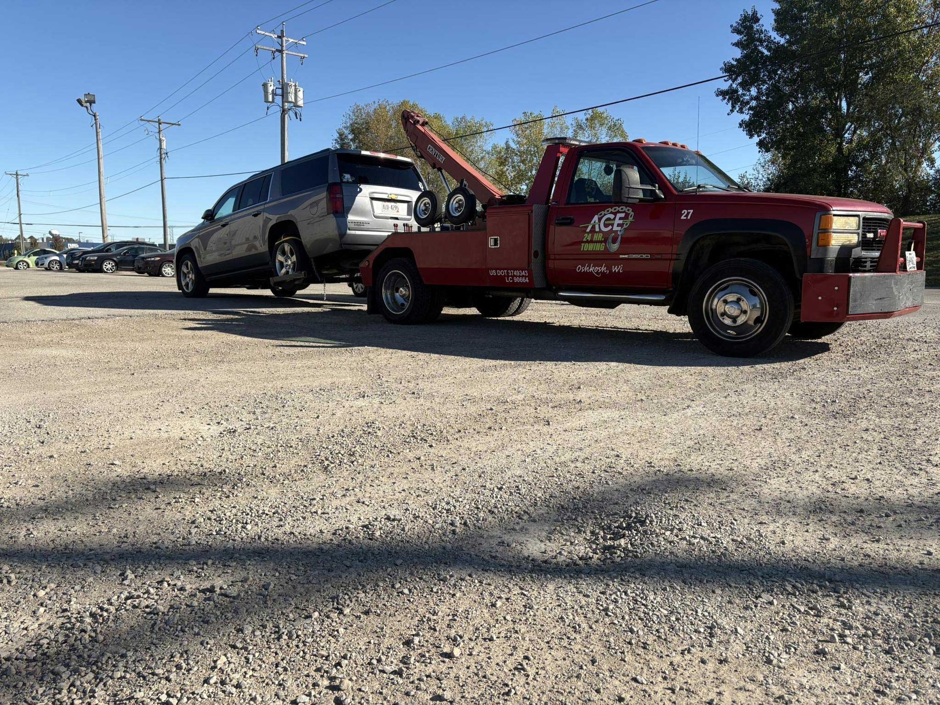 Red tow truck hauling a gray SUV on a gravel lot under a clear blue sky