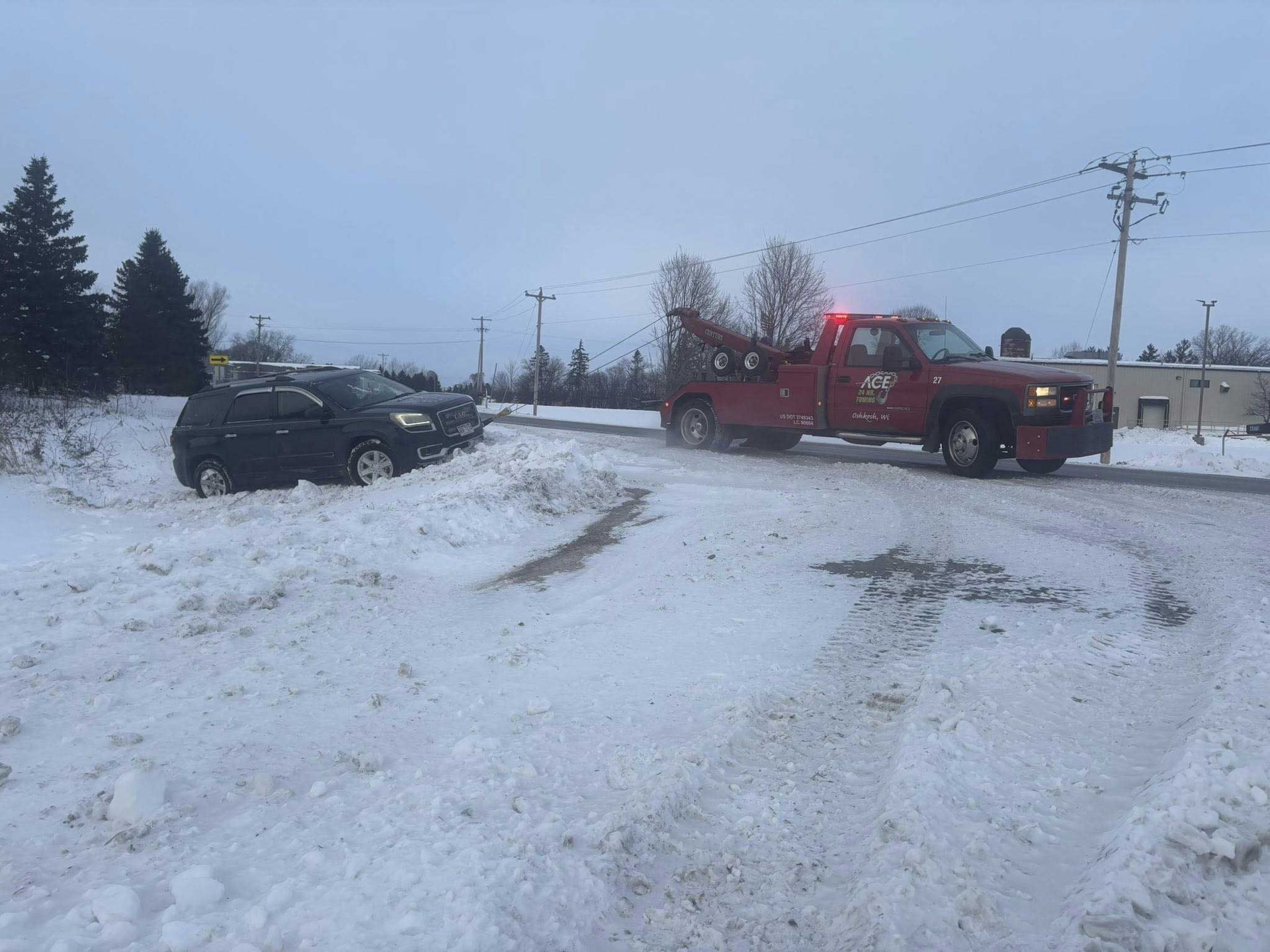 Red tow truck pulling a black car on a snowy roadside under a gray sky.