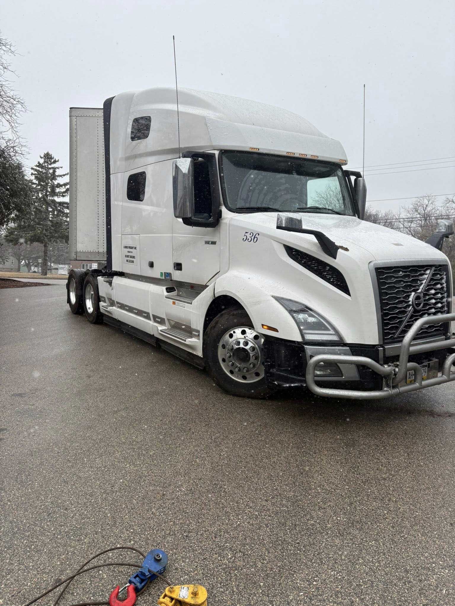 White semi-truck parked on a snowy roadside, viewed from the front-left.