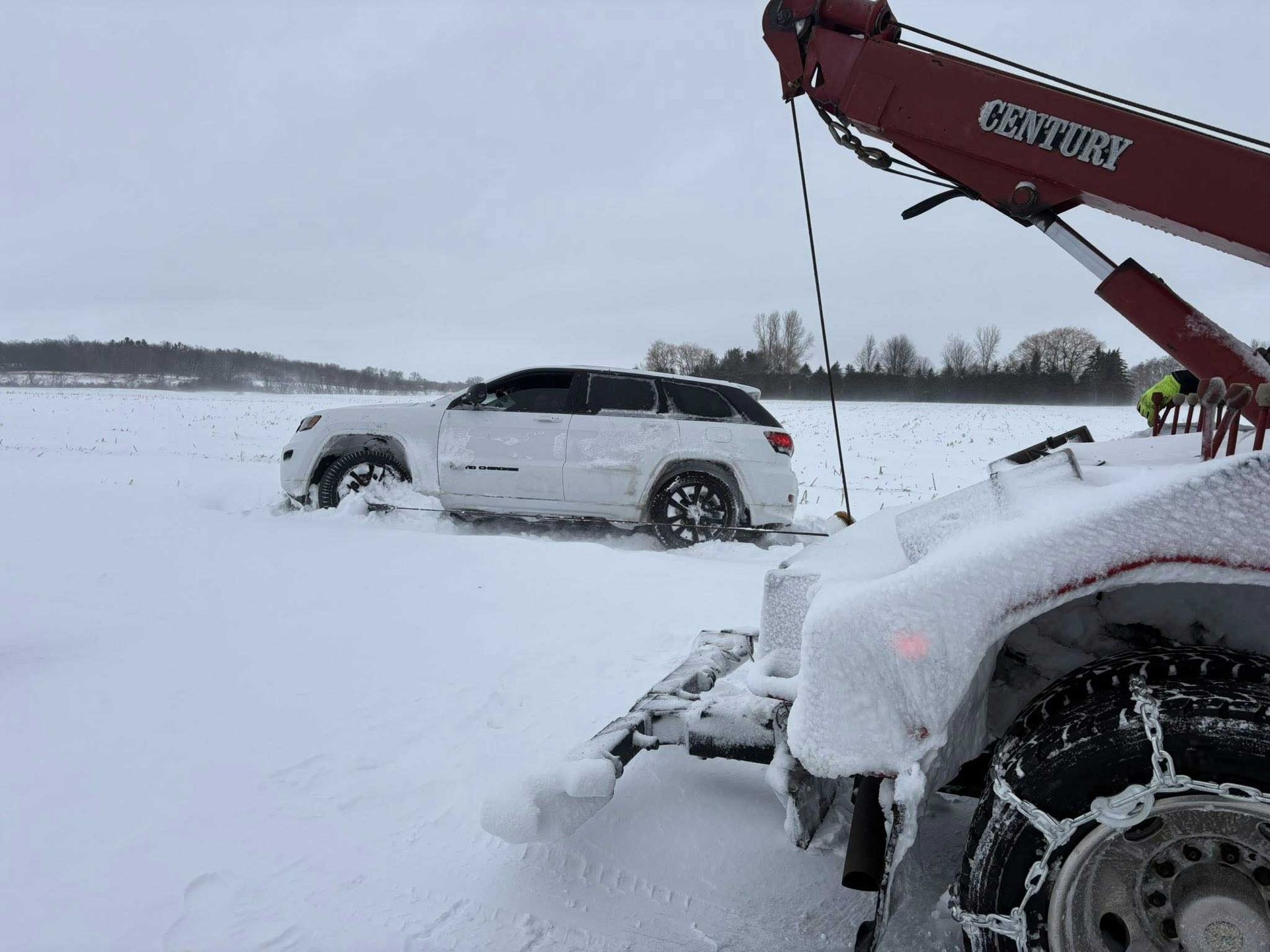 Snow-covered SUV stuck in a snowy field, with a tow truck arm in the foreground.