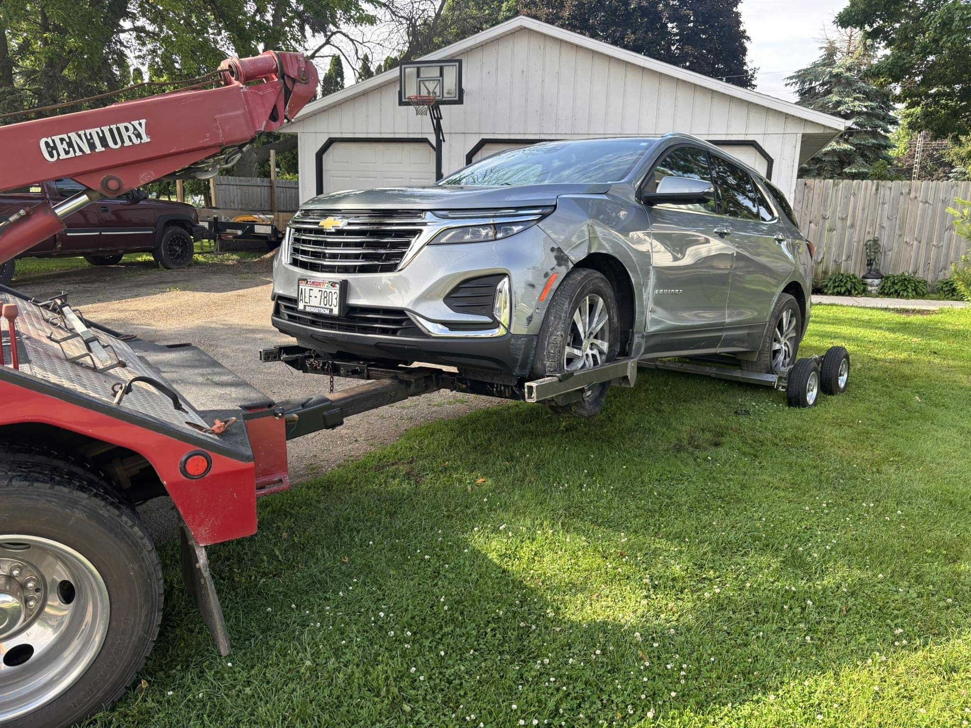Silver SUV being towed by a red tow truck in a grassy yard beside a house.