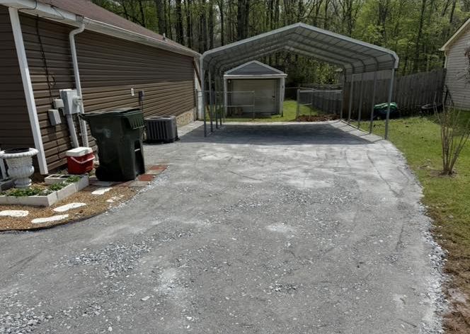 Gravel driveway with a metal carport, trash can, and side of a house.