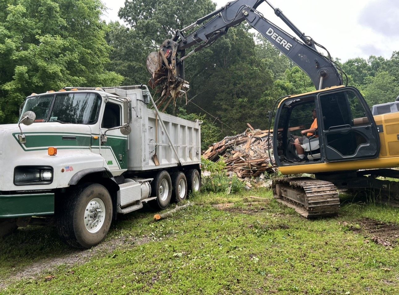 A dump truck is being loaded with logs by an excavator.