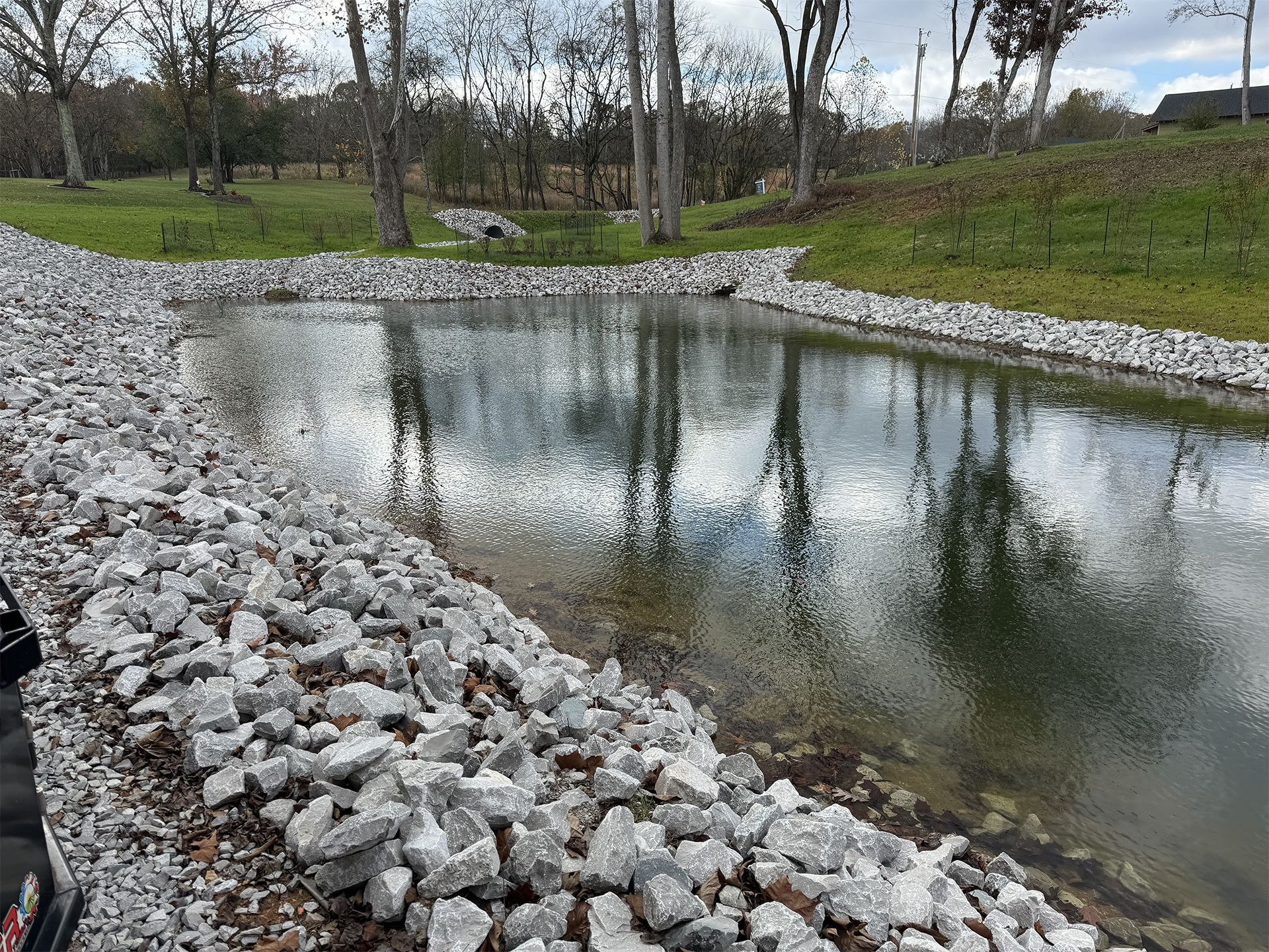 A pond surrounded by rocks and trees with a reflection of trees in the water.