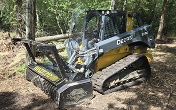 Yellow and gray John Deere compact track loader with a Diamond mulching head clearing brush in a wooded area.