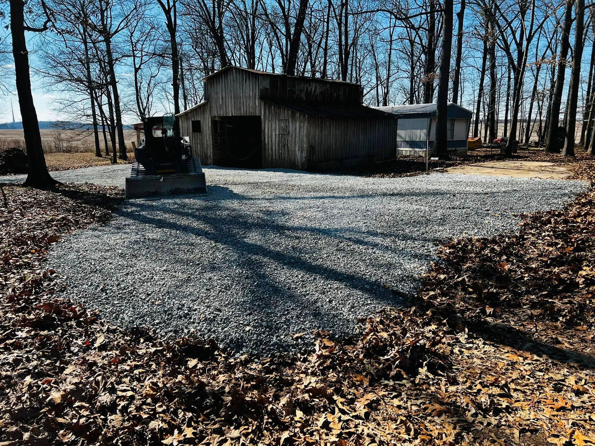 A gravel driveway leading to a barn in the woods