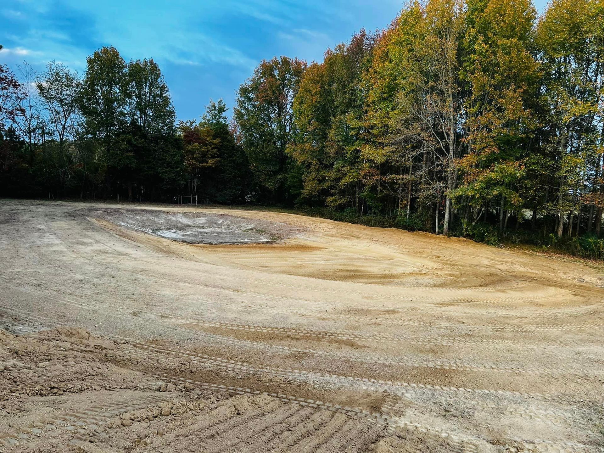 A dirt field with trees in the background and a blue sky