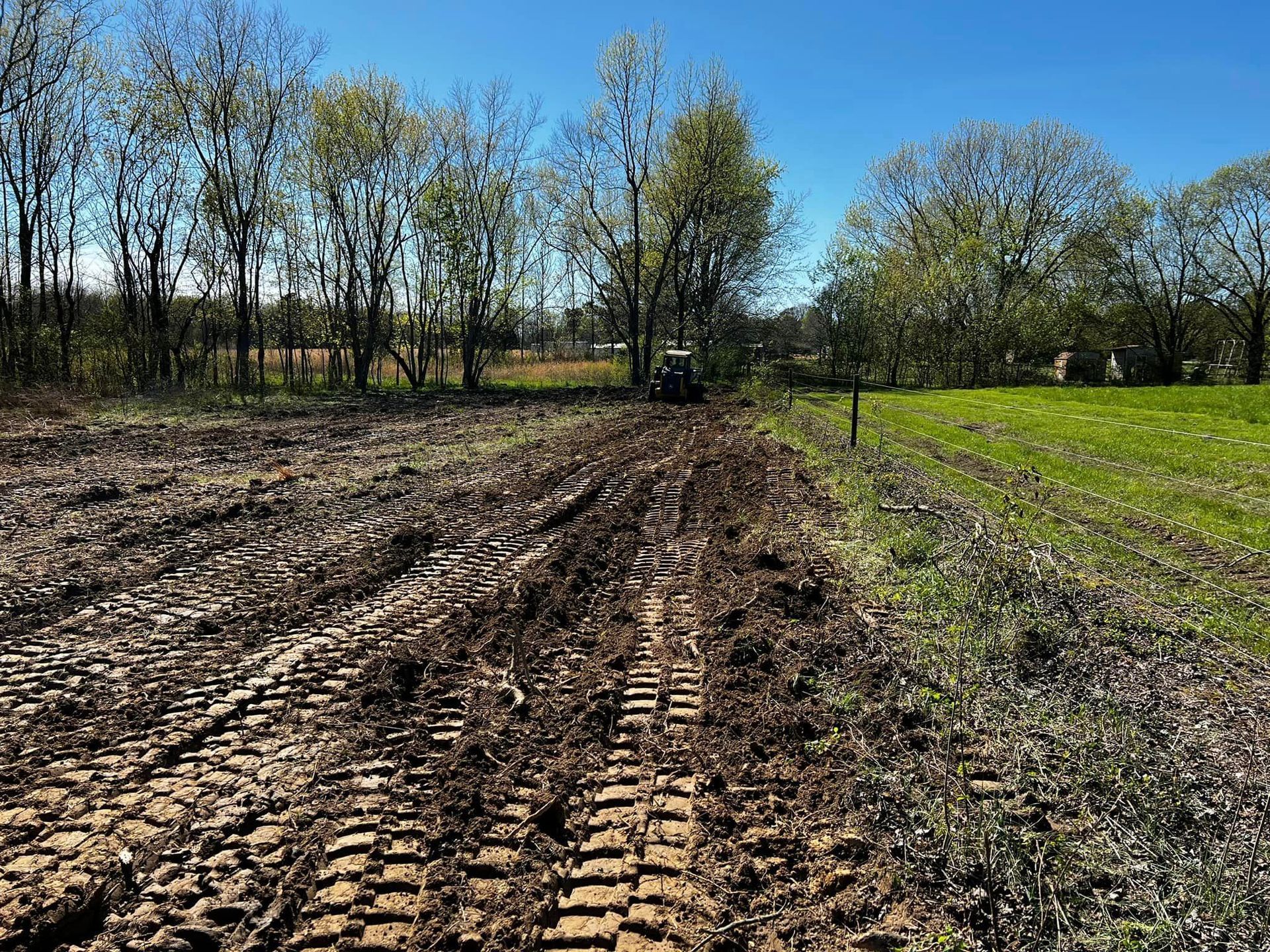 A tractor is plowing a muddy field with trees in the background.