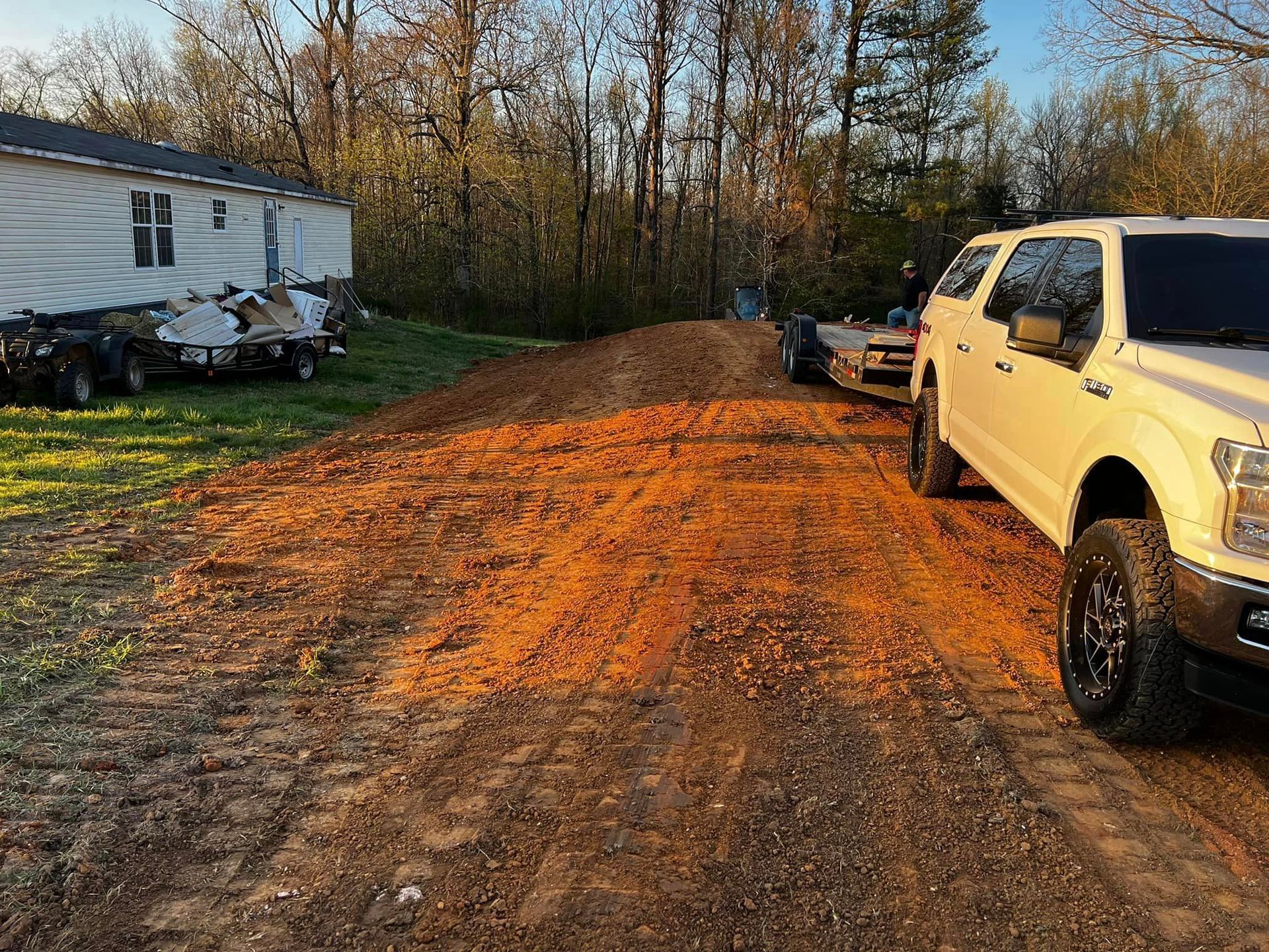 A white truck is parked on a dirt road next to a trailer.