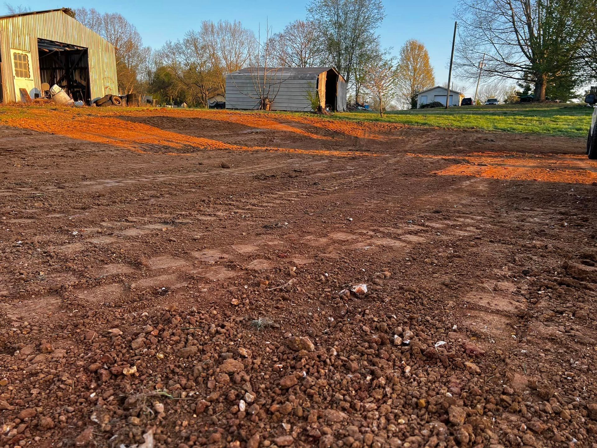 A car is parked in a dirt field with a barn in the background.