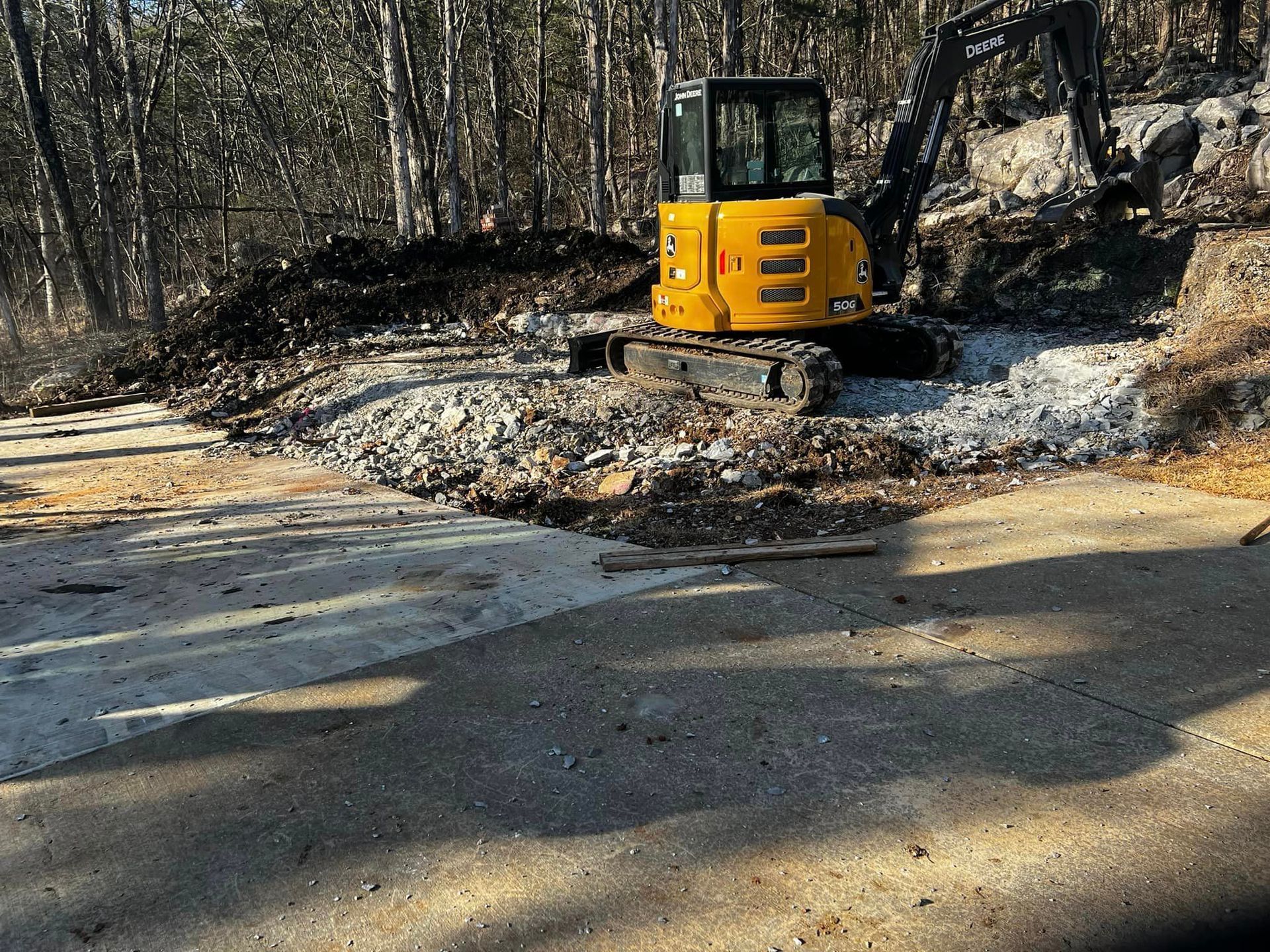A yellow excavator is driving down a dirt road in the woods.