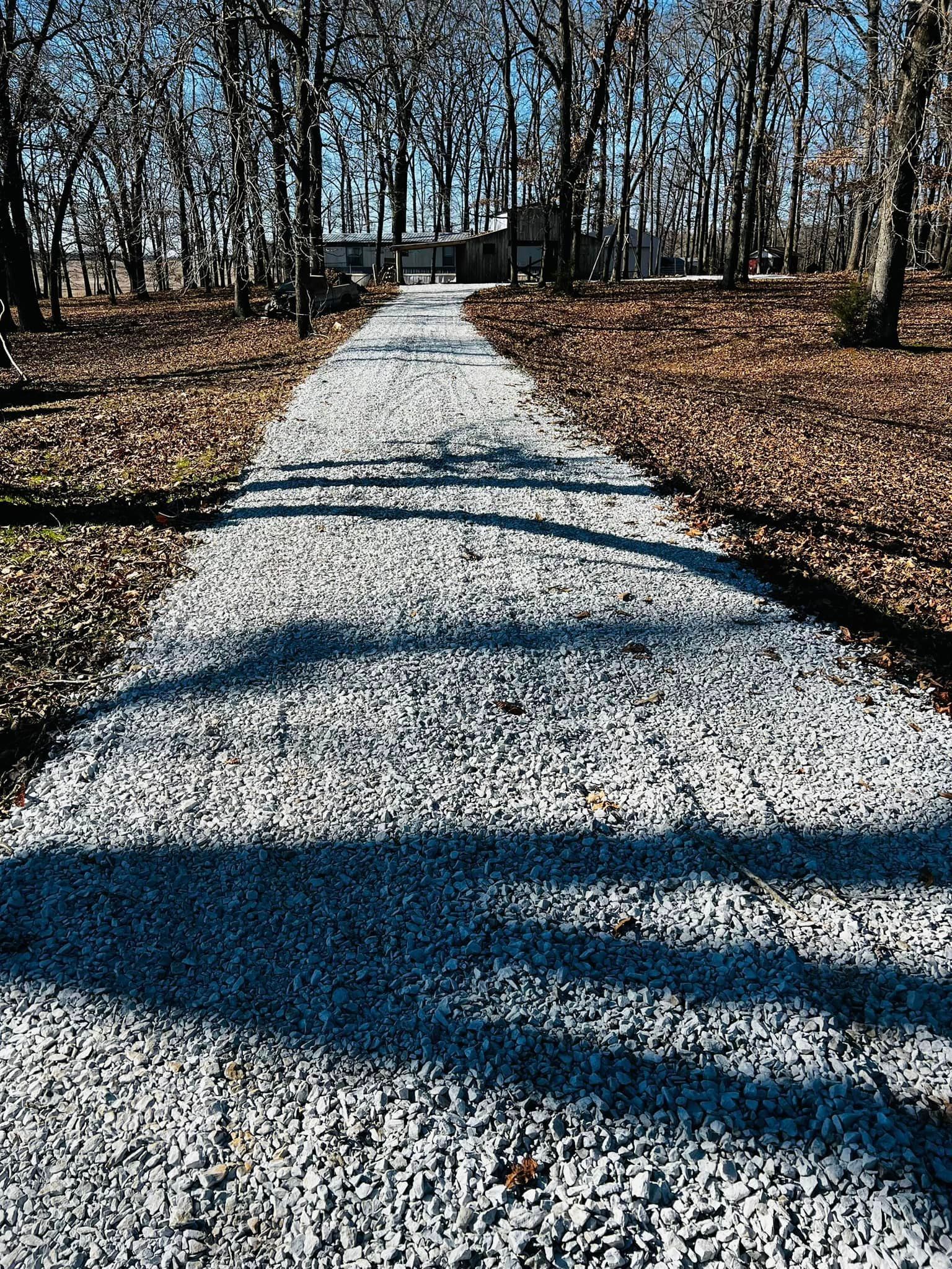 A gravel driveway leading to a house in the woods.