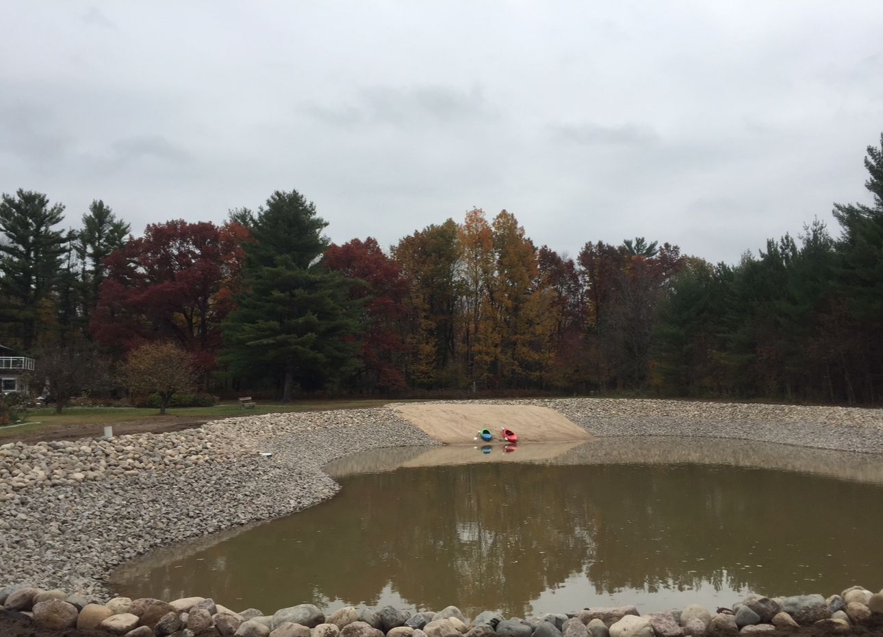 Pond surrounded by rocks and trees with autumn foliage under a cloudy sky.