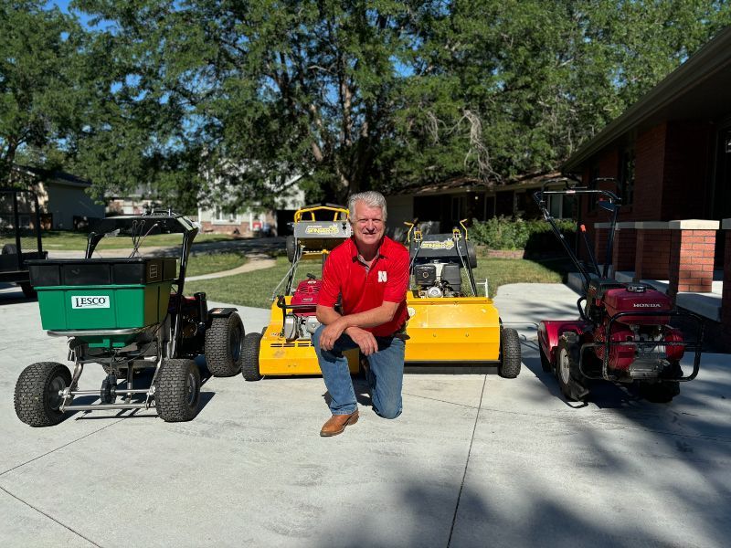 A man in a red shirt is kneeling in front of a lawnmower.