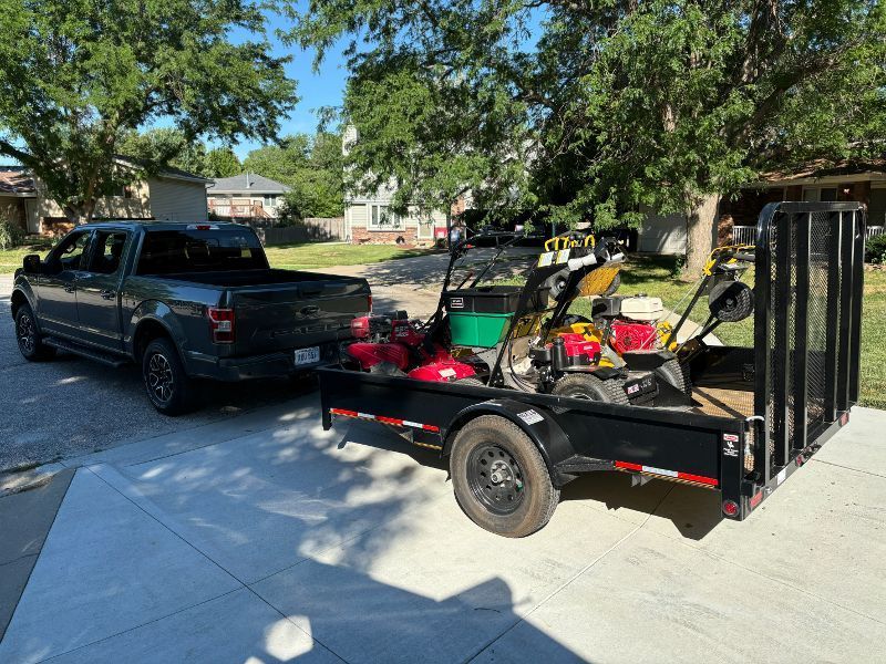 A truck is towing a trailer with a lawn mower on it.