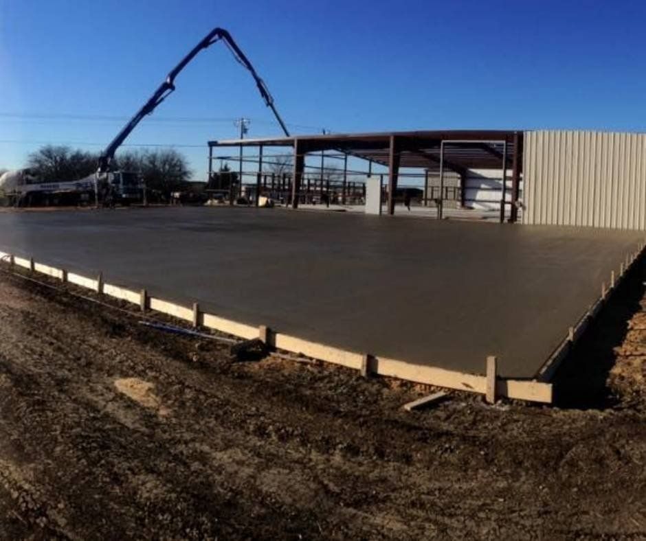 A large concrete slab is being poured in front of a building under construction