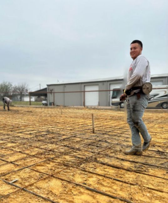 A man is standing in a dirt field holding a hammer.
