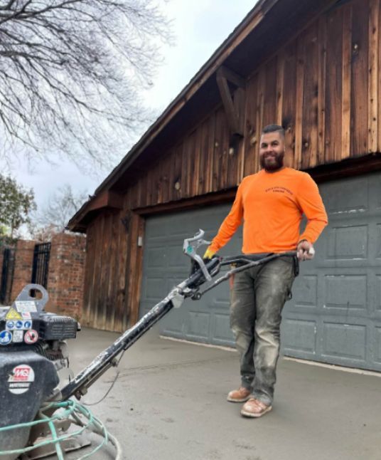 A man in an orange shirt is standing next to a machine in front of a garage door.