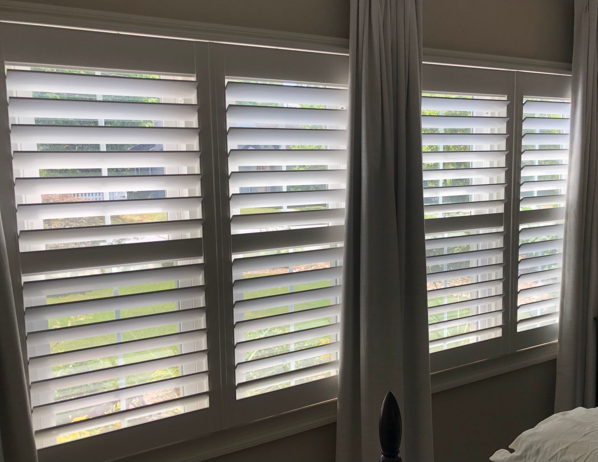 A bedroom with white shutters on the windows and white curtains.