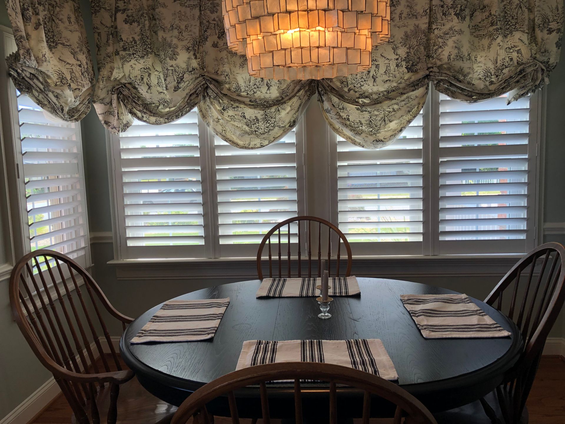 A dining room with a table and chairs and shutters on the windows.