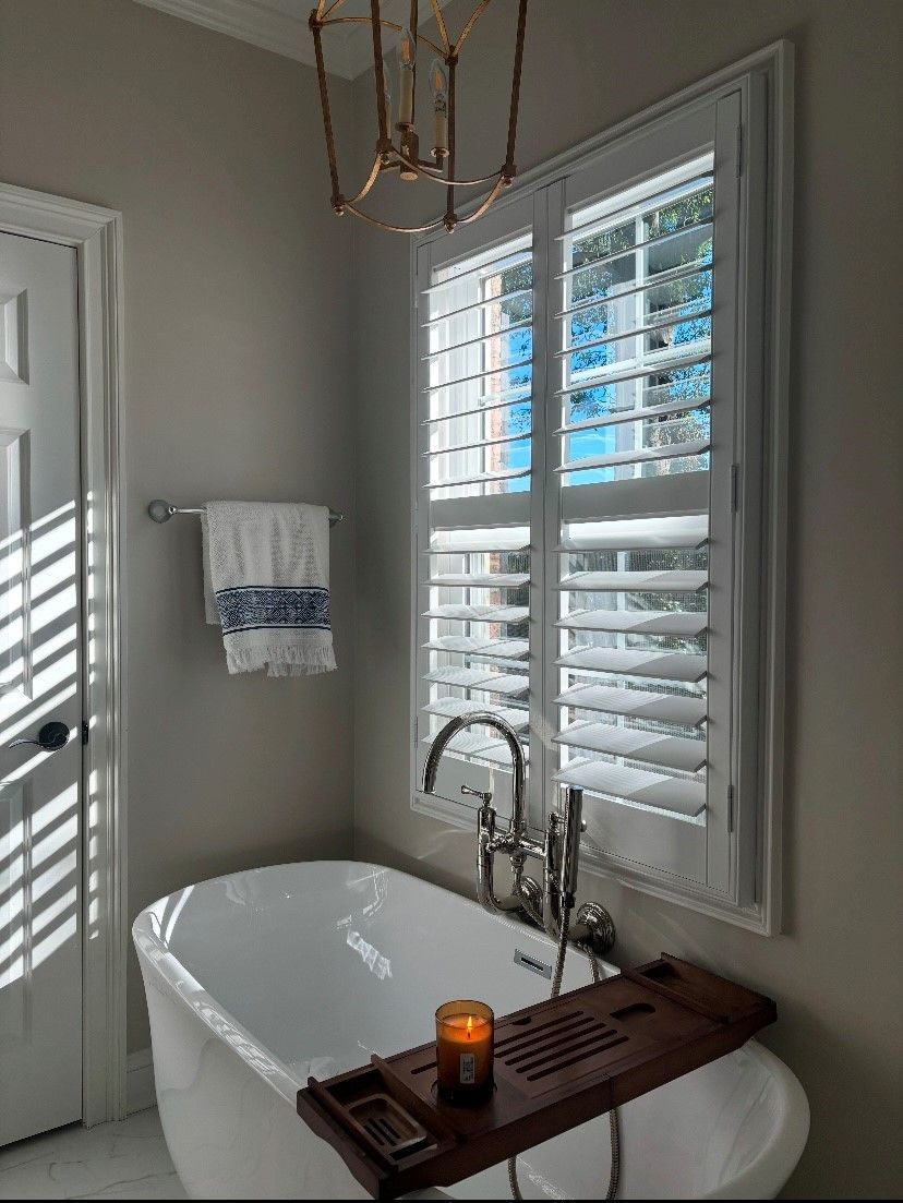 There is a bathtub in the bathroom with shutters on the windows.