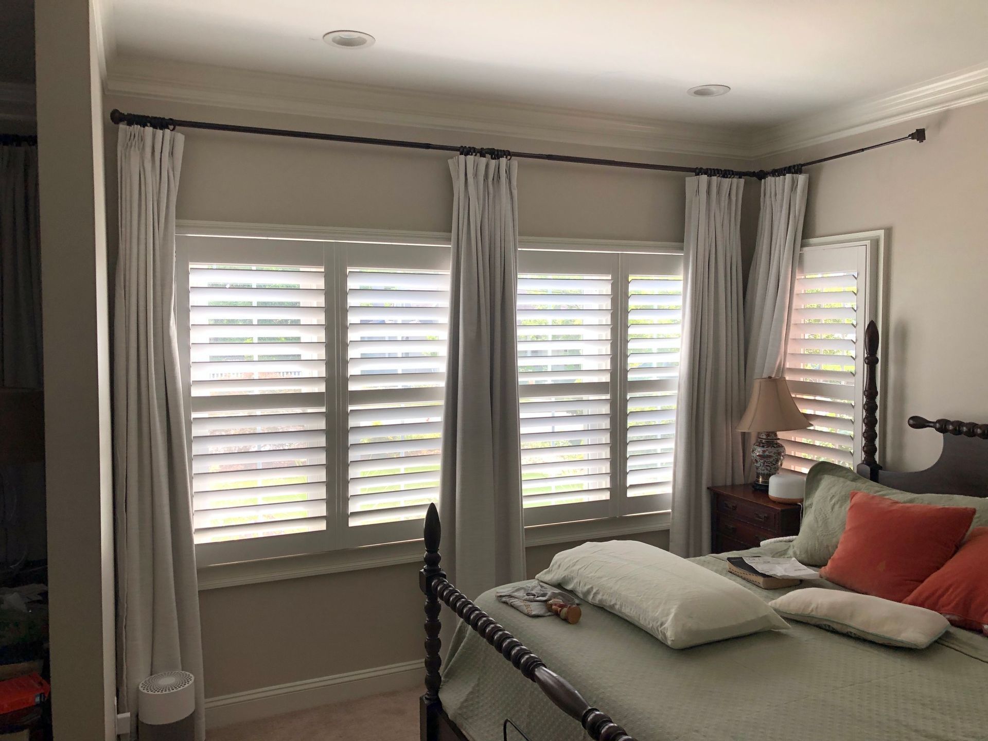 A bedroom with a bed, curtains, and shutters on the windows.