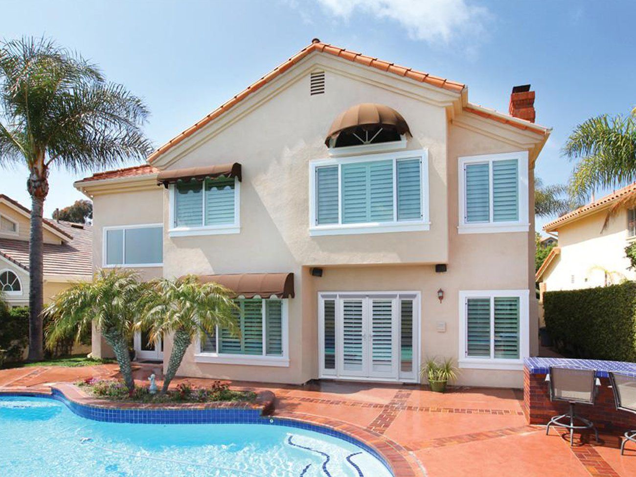 Two-story stucco house with pool, palm trees, and a red-tiled patio