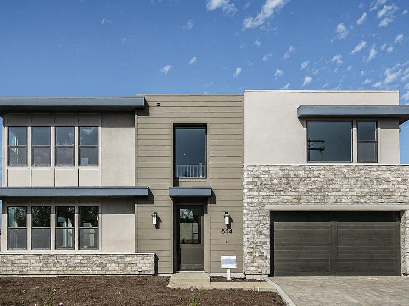 Modern two-story house with beige siding, stone facade, and a double garage under a blue sky