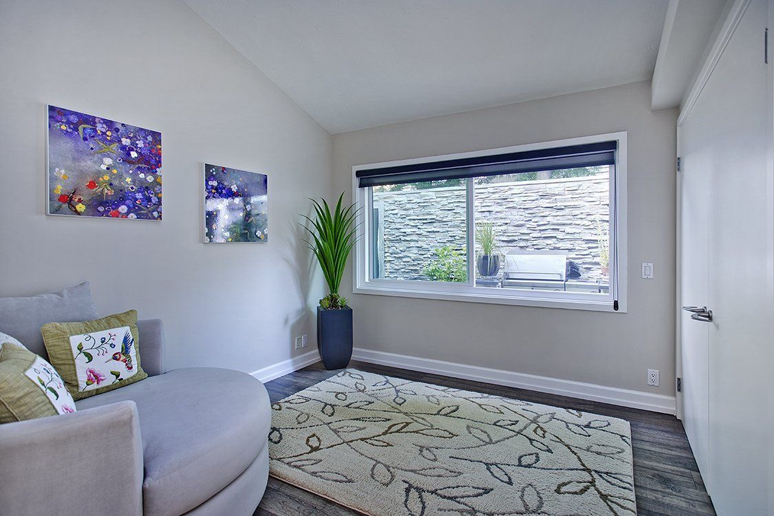 Bright living room with gray sofa, patterned rug, wall art, large window, and potted plant