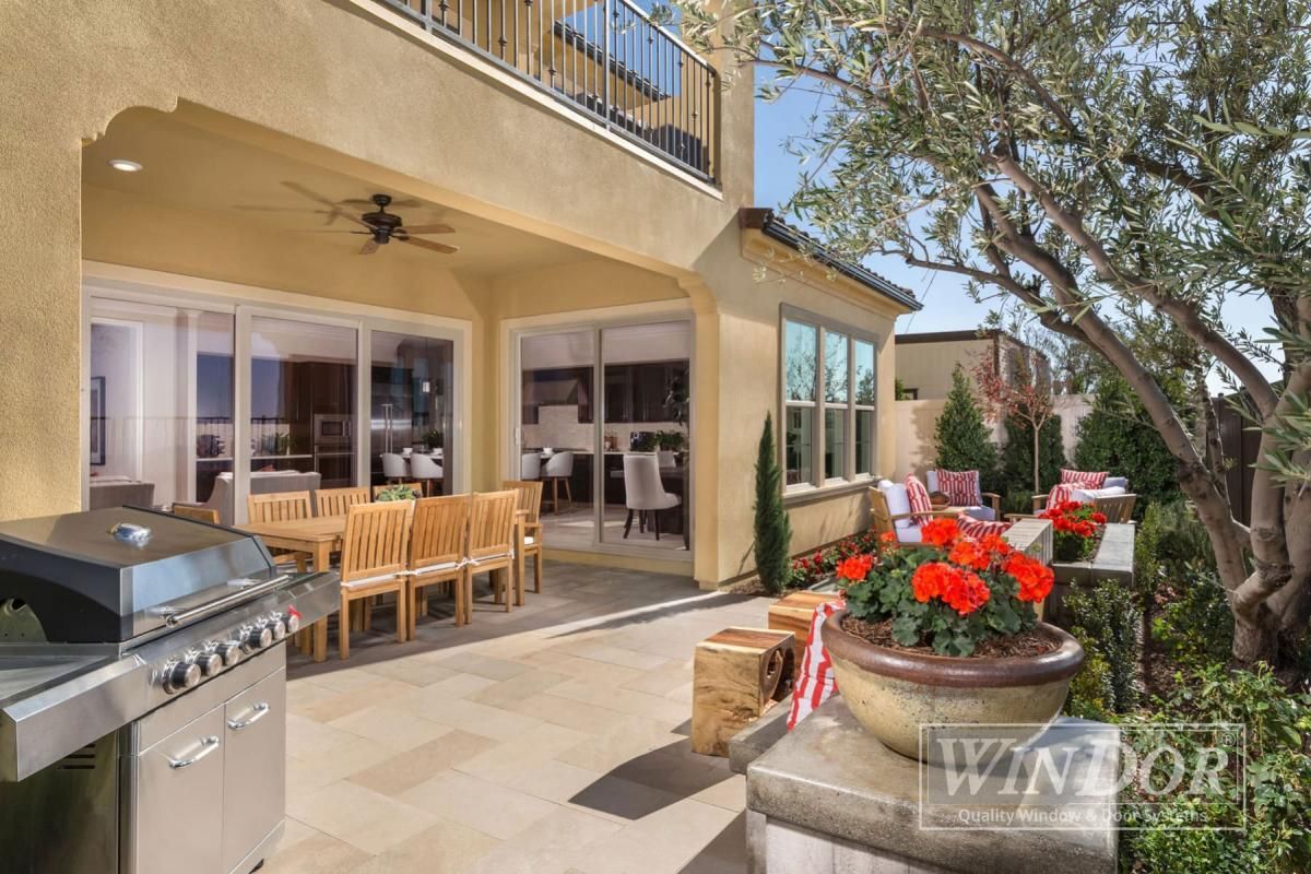 Patio with grill, wooden dining table, sliding doors, and flower planter beside a tree