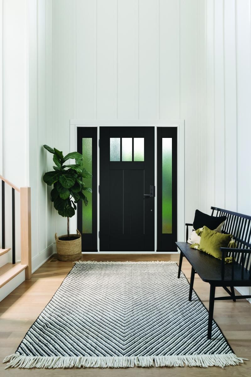 Modern entryway with black door, bench, potted plant, and striped rug on a light floor