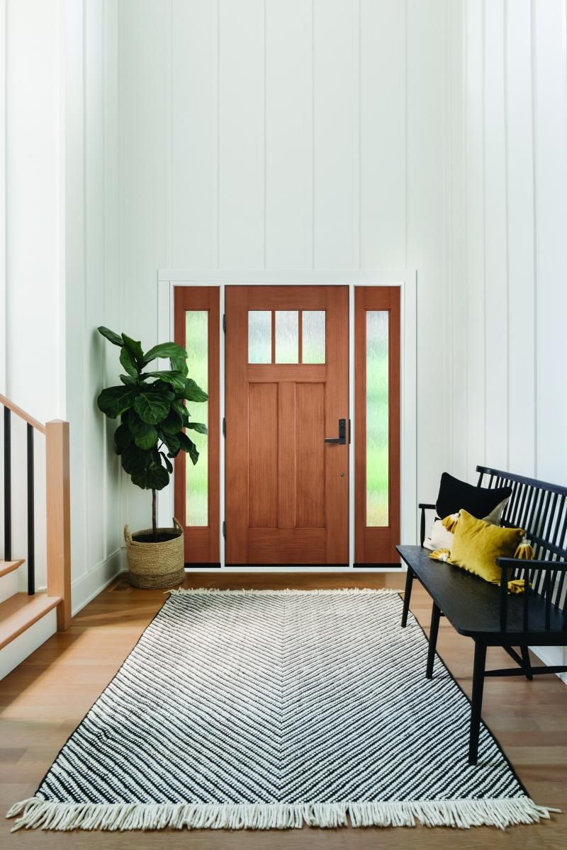 Modern entryway with wooden front door, black bench, potted plant, and striped rug