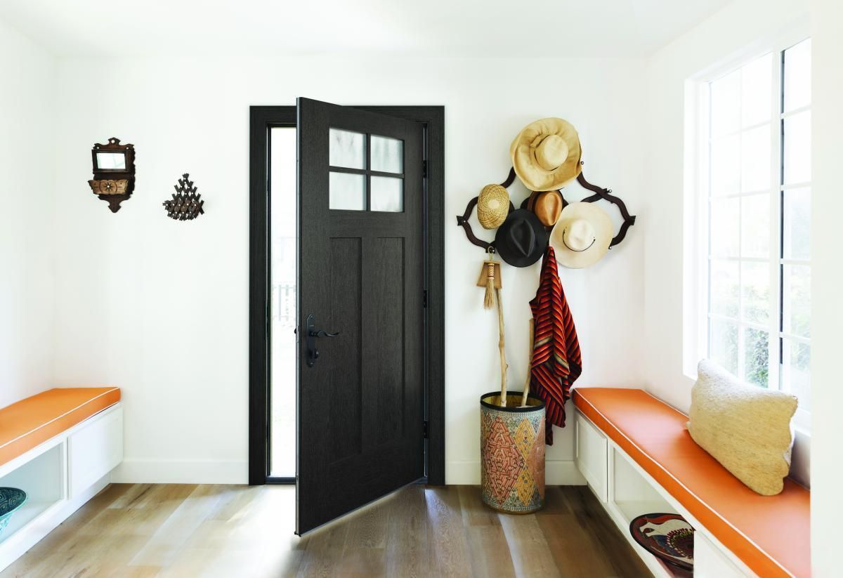 Bright entryway with a black door, orange benches, wall hooks with hats, and a window on the right.