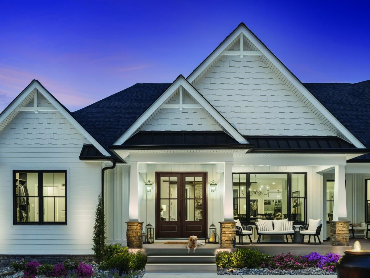 White suburban house with lit porch and front yard at dusk